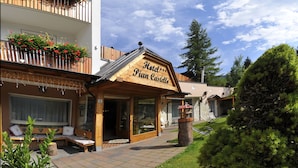 A hotel entrance with a wooden sign, outdoor seating, and a garden area. - Hotel Pian Castello (Andalo)