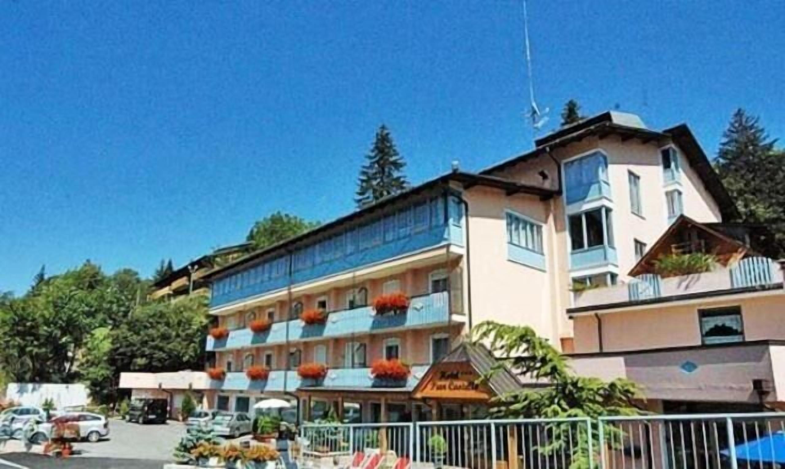 Un hotel de varios pisos, con balcones adornados con macetas de flores naranjas y un letrero que indica un restaurante en la planta baja.