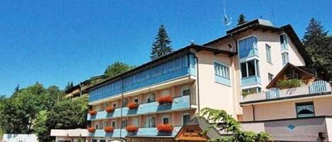 Un hotel de varios pisos, con balcones adornados con macetas de flores naranjas y un letrero que indica un restaurante en la planta baja.