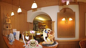 A reception area with a wooden counter, a telephone, a decorative lamp, and a wall-mounted light fixture. - Hotel Pian Castello (Andalo)