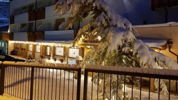 A hotel with a snow-covered exterior and a well-lit entrance. - Hotel Pian Castello (Andalo)