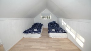 A small attic bedroom with two beds, a sloped ceiling, and a small window.
