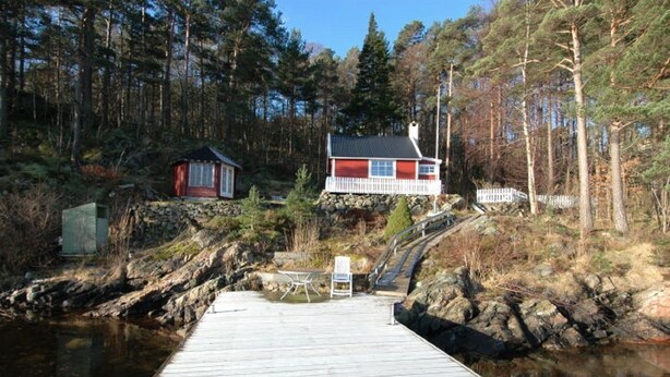 A wooden dock leading to a house with a red roof, surrounded by a forest.