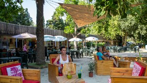 Outdoor seating with umbrellas, wooden furniture, and a sandy ground. - Camping Du Pont D'Avignon (Avignon)