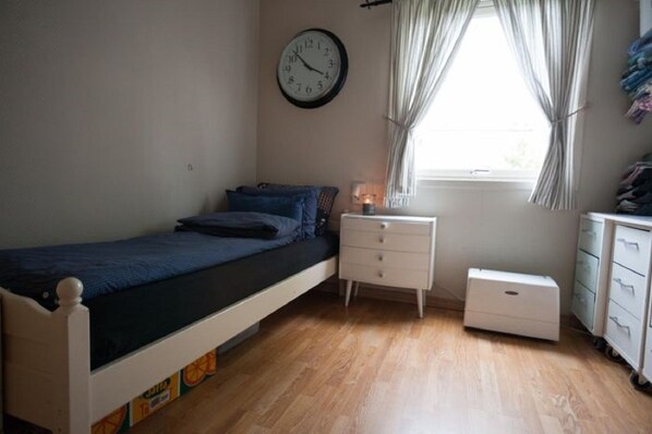 Un dormitorio con cama, mesita de noche, cómoda, reloj y ventana con cortinas.