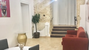 A modern living space with a dining area, a red sofa, a staircase, and a large plant. - Palazzo delle Logge (Palermo)
