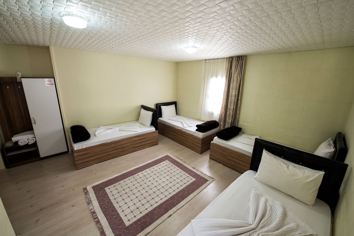 A hotel room with two single beds, a large rug, a wardrobe, and a refrigerator.