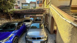 A parking area with two cars, a building with a textured wall, and a staircase. - Yellow Rose Pansiyon (Çanakkale)