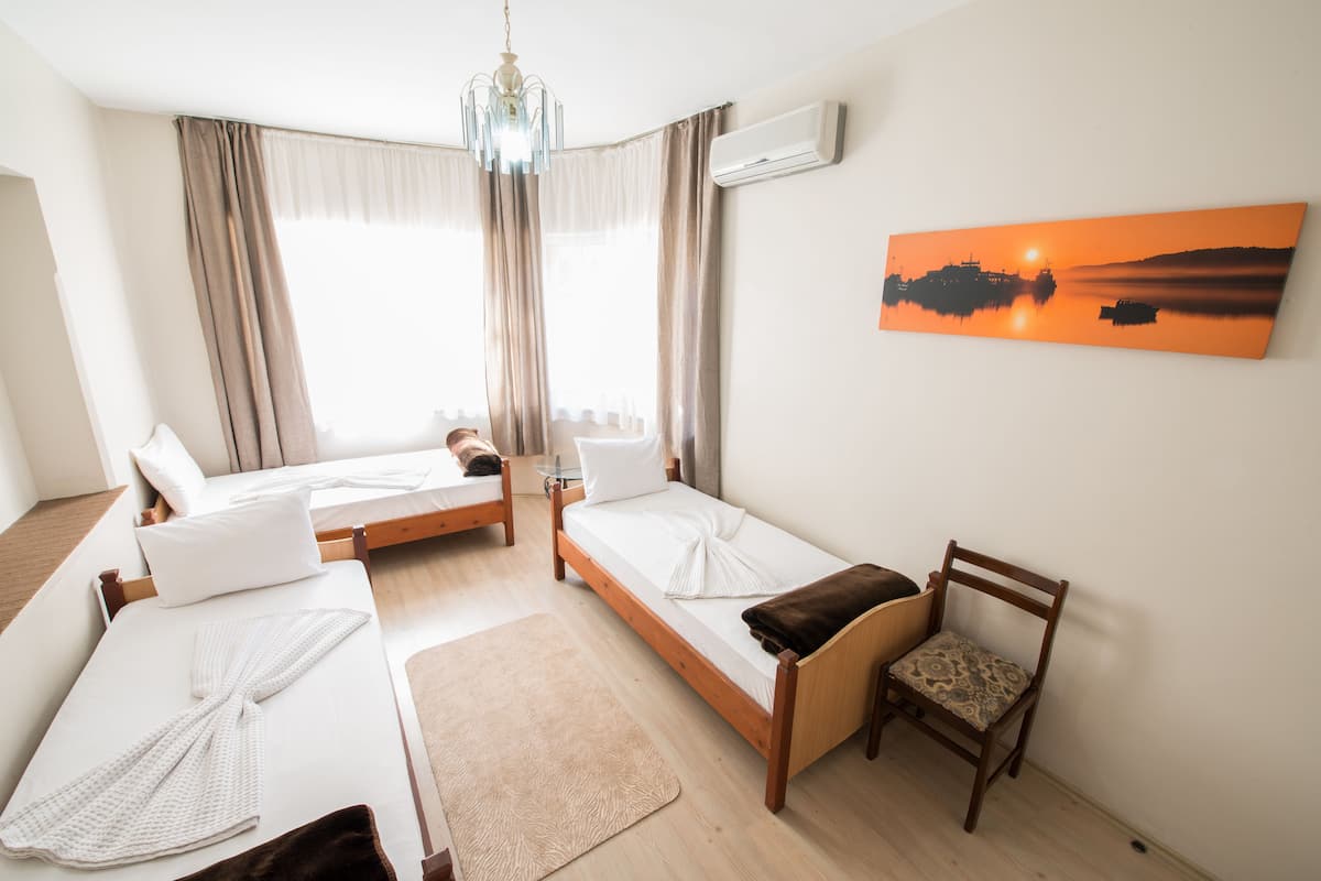A hotel room with two single beds, a wooden chair, a painting on the wall, and a chandelier.