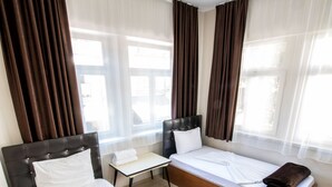 A hotel room with two beds, a small table, and a window with curtains. - Yellow Rose Pansiyon (Çanakkale)