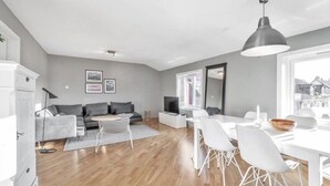 Ein modernes Wohnzimmer mit einem grauen Sofa, einem Esstisch mit weißen Stühlen und einem großen Fenster.