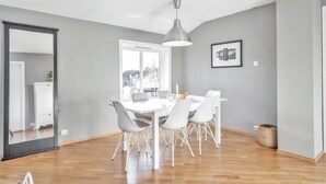 Ein moderner Essbereich mit einem weißen Tisch und Stühlen, einer Pendelleuchte und Blick durch ein großes Fenster.