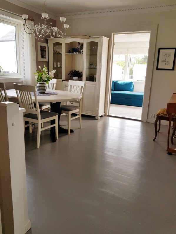 Uma área de refeições com mesa e cadeiras brancas, um lustre e vista para o exterior.