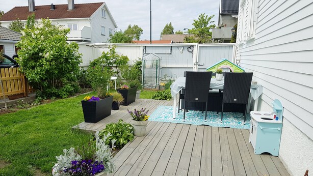 Ett trädäck med utemöbler, krukväxter och ett litet lekstuga.