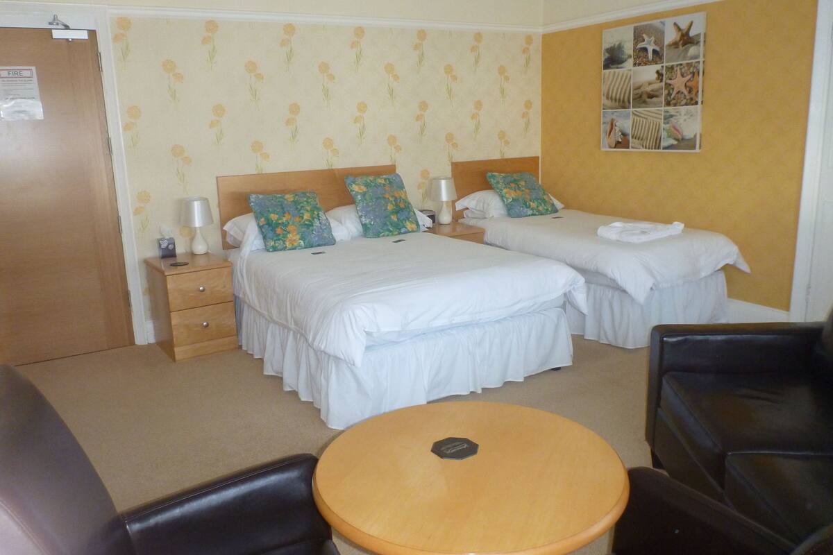A hotel room with two beds, a wooden nightstand, a round table, and a black leather chair.