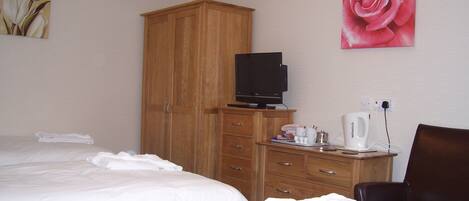 A hotel room with two beds, a wooden wardrobe, a television, a coffee maker, and a chair.