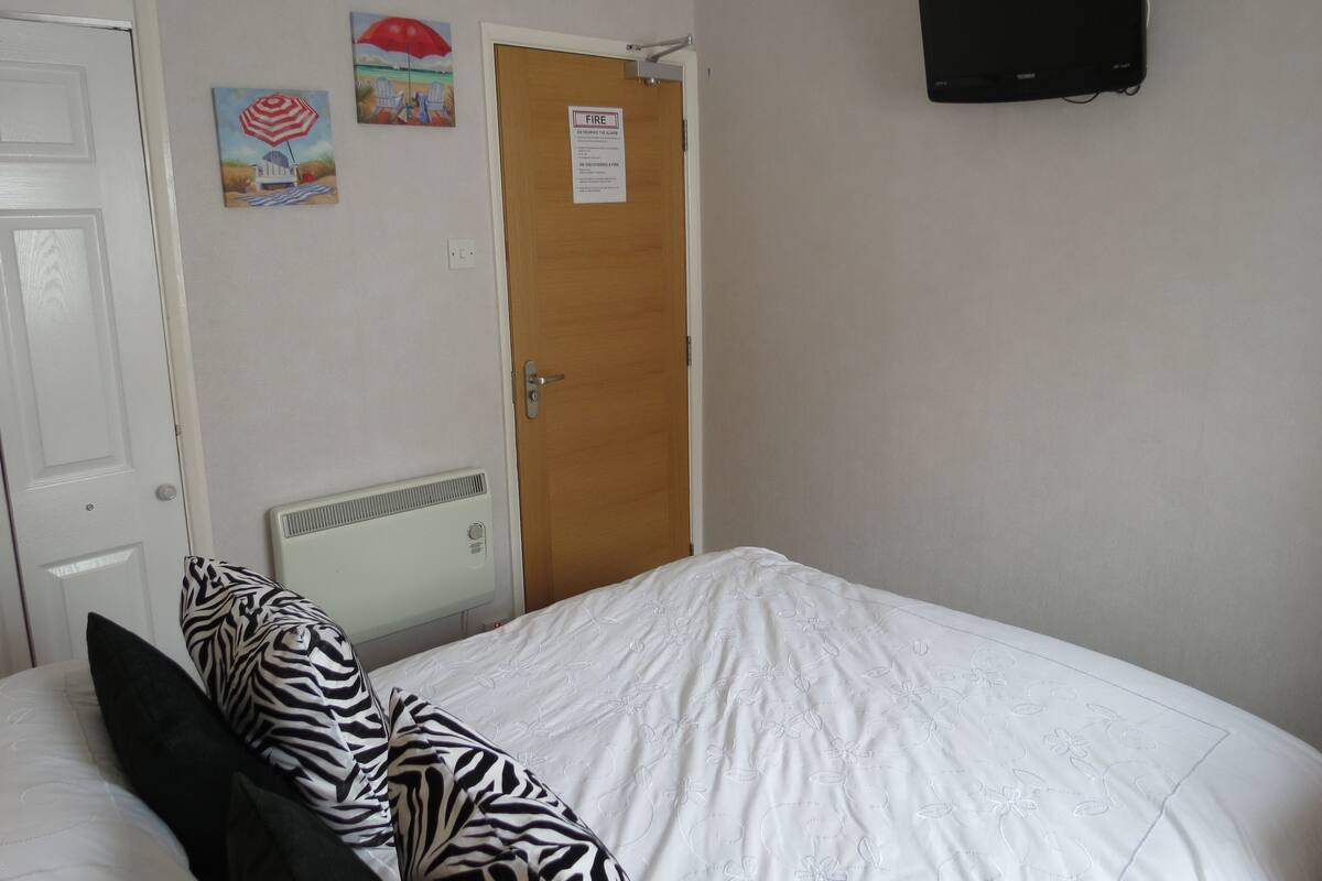 A bedroom with a bed, a radiator, a TV, and a door with a fire safety sign.