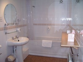 Un baño con lavamanos, espejo, bañera y un perchero para toallas.