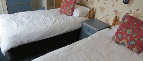 A hotel room with two beds, a desk with a computer, and a small table with a kettle and cups.