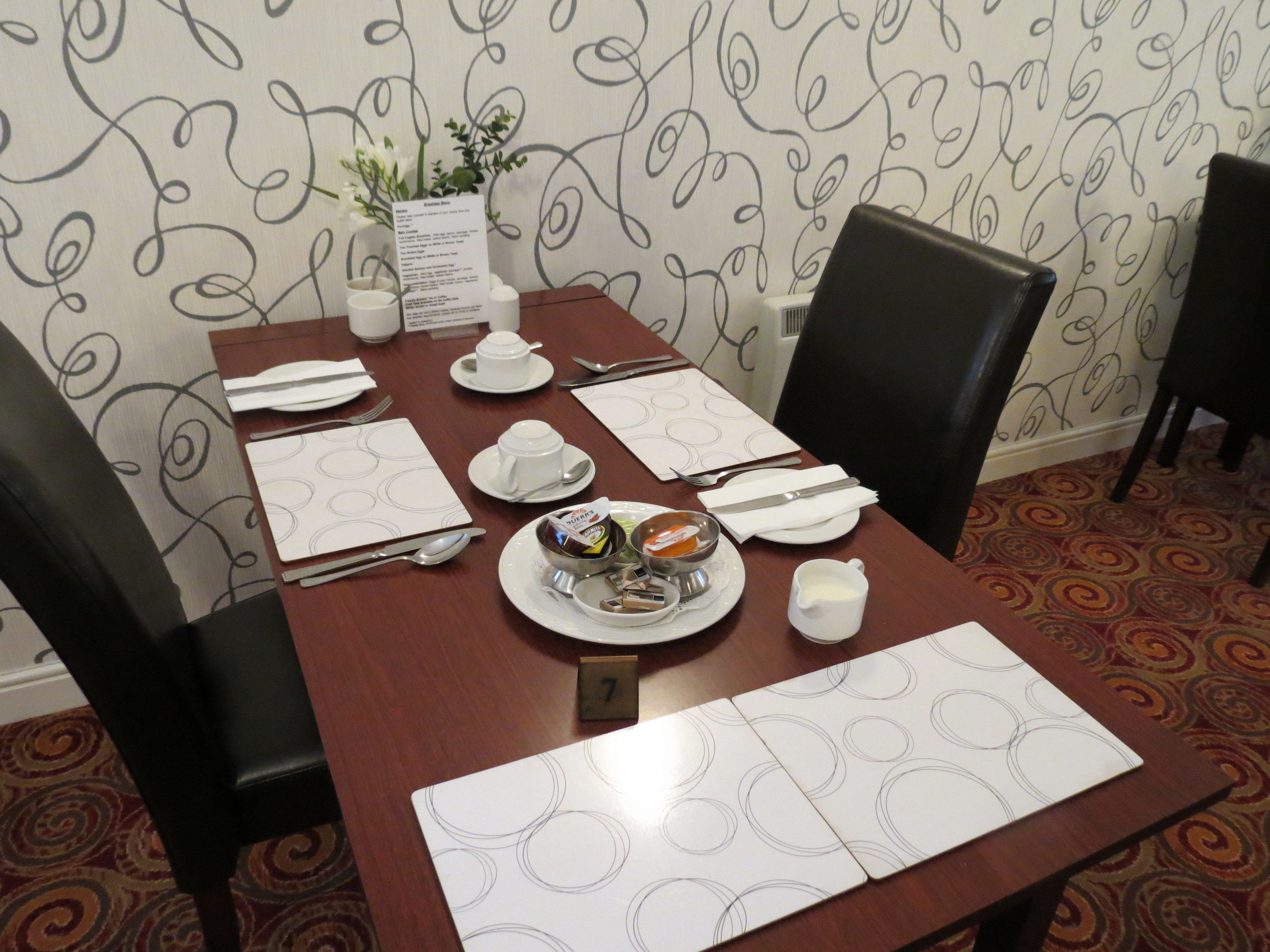 A dining table set with plates, bowls, cutlery, and a menu.