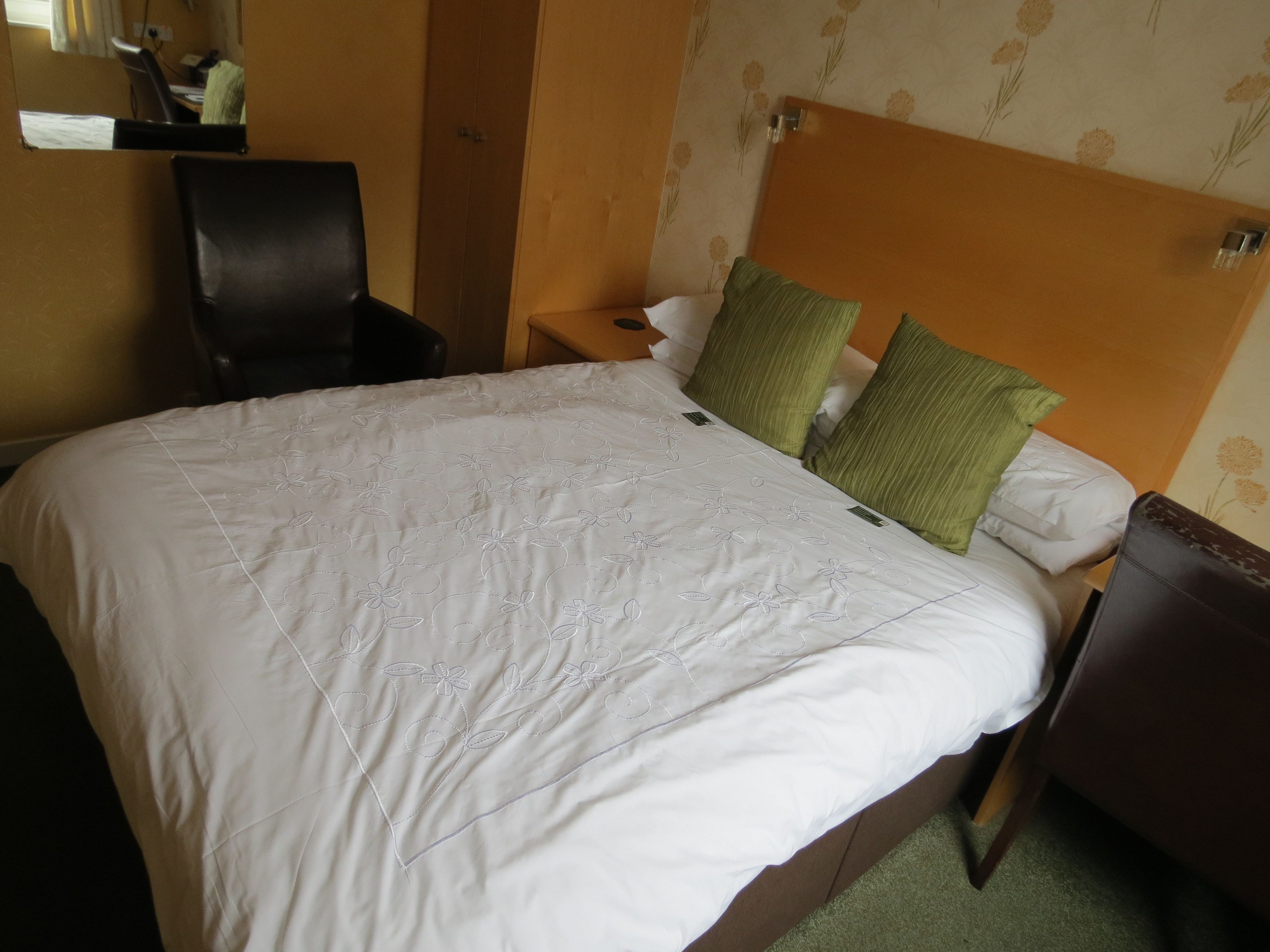 A hotel room with a large bed, a chair, a nightstand, and a mirror.