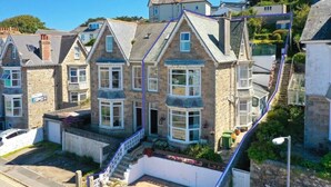 A row of stone houses with pitched roofs, a central entrance with a staircase, and a small garden area. - Harbour View Guest House (St Ives)