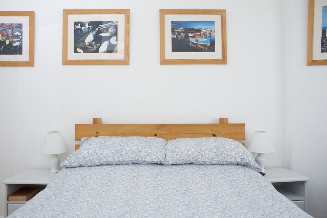 Une chambre à coucher avec une tête de lit en bois, un lit recouvert d’une couette à motifs, deux tables de chevet avec des lampes et trois photographies encadrées accrochées au mur.