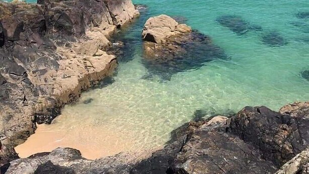 A coastal scene with clear turquoise waters, rocky formations, and a distant shoreline with buildings and a lighthouse. - Harbour View Guest House (St Ives)