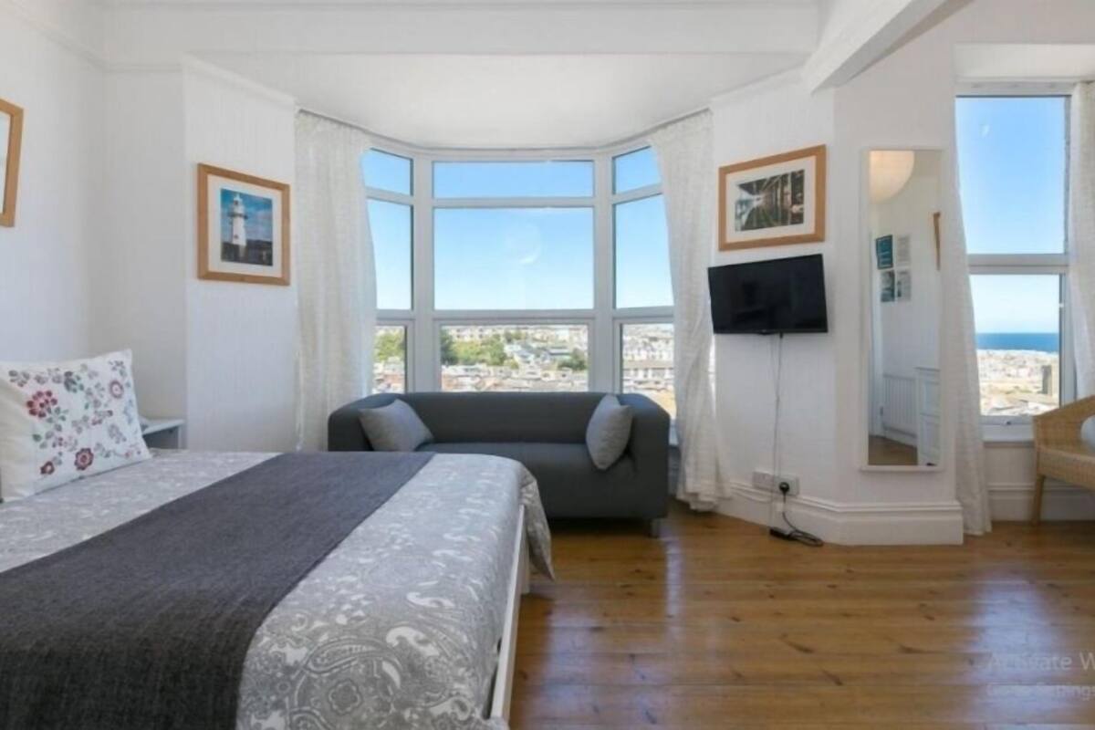 Ein Schlafzimmer mit Bett, einer Couch, einem Fernseher und großen Fenstern mit Blick.