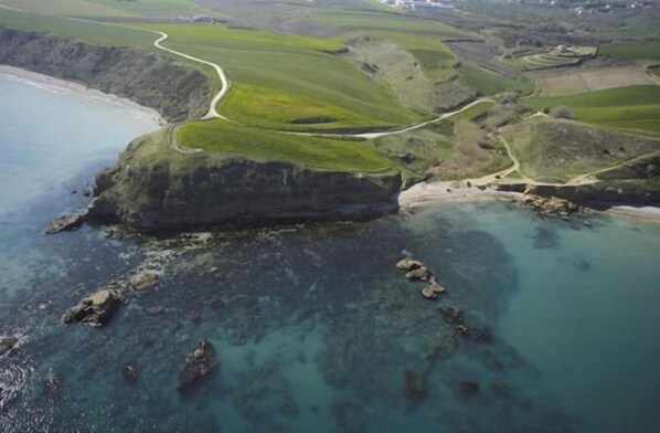 An aerial view of a coastal landscape with a winding road, green fields, and rocky terrain. - Villa Istonia (Cupello)