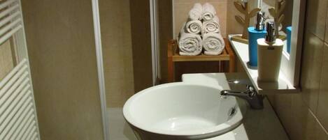 A bathroom with a white sink, a shower, and a towel rack with neatly folded towels.