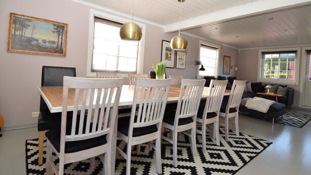A dining area with a wooden table and white chairs, a black and white rug, and pendant lights. - Solferie Holiday Home Jolleveien (Kristiansand)