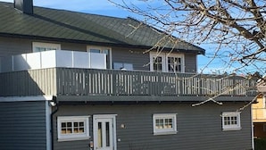 A two-story house with a balcony, a front door, and a small patio area. - Solferie Holiday Home Jolleveien (Kristiansand)