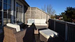 A covered outdoor seating area with wicker furniture and a wooden deck. - Solferie Holiday Home Jolleveien (Kristiansand)