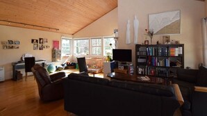 A spacious living room with wooden flooring, a large bookshelf, and a comfortable seating area. - Solferie Holiday Home Breimyråsen (Kristiansand)