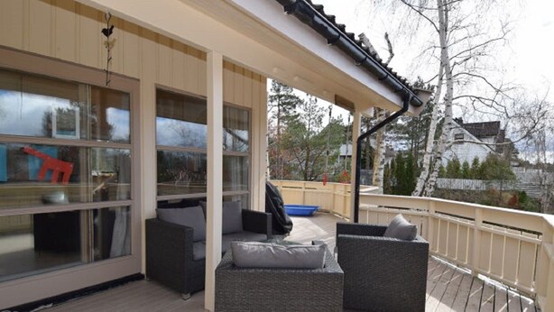 An outdoor deck with wicker furniture, a blue pool, and a view of the surrounding area. - Solferie Holiday Home Breimyråsen (Kristiansand)