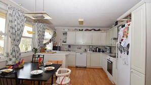 A compact kitchen with white cabinets, a dining table with chairs, and a refrigerator with magnets. - Solferie Holiday Home Breimyråsen (Kristiansand)