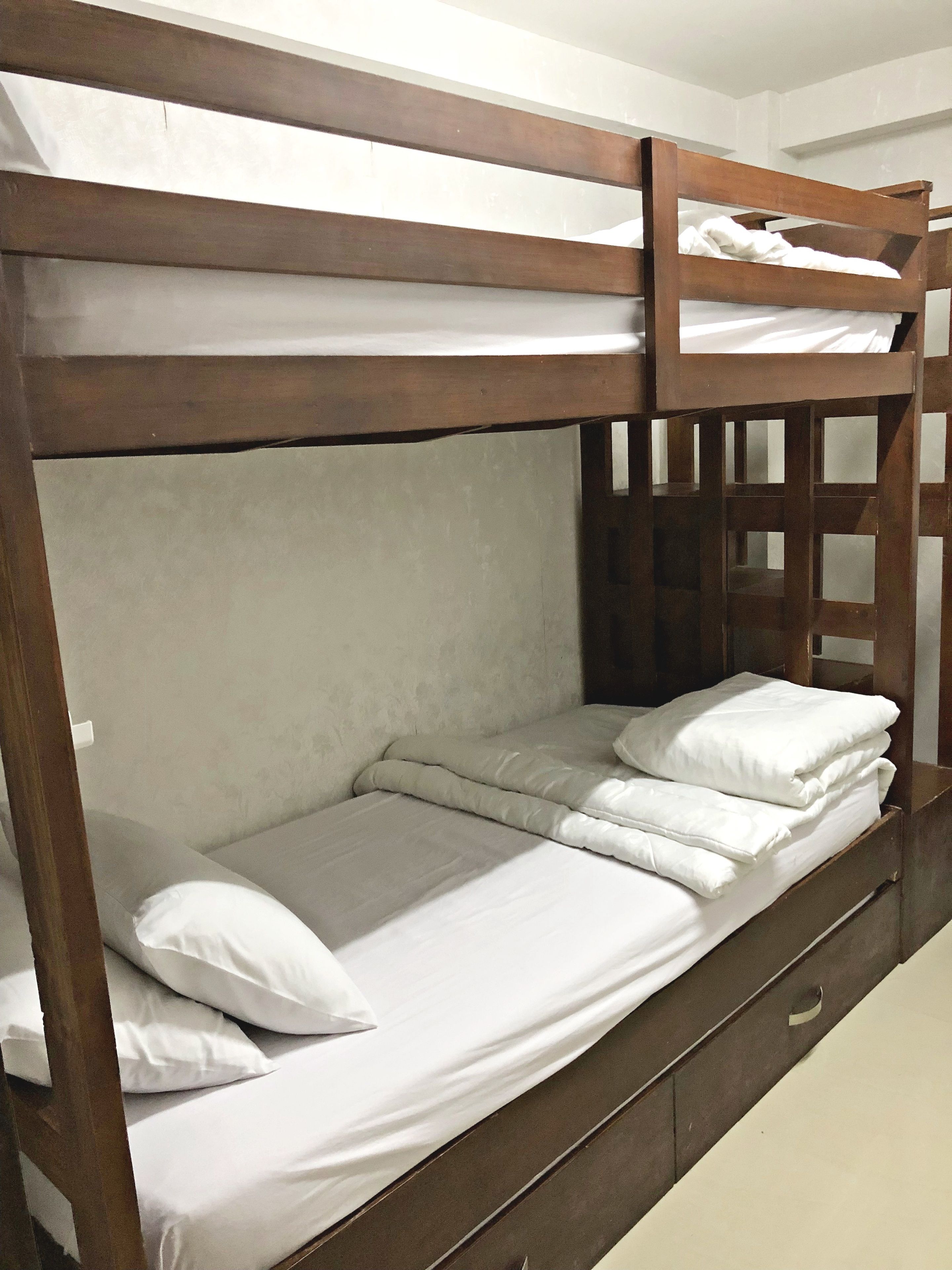 Una litera con estructura de madera, ropa de cama blanca y cabecera con diseño de cuadrícula.