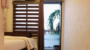 A hotel room with a bed, a small table, a window with blinds, a TV mounted on the wall, and a view of the outside.