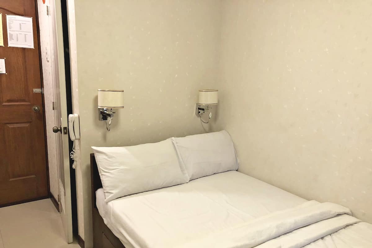 A small, neatly made bed with white linens in a room with light-colored walls and a wooden door.