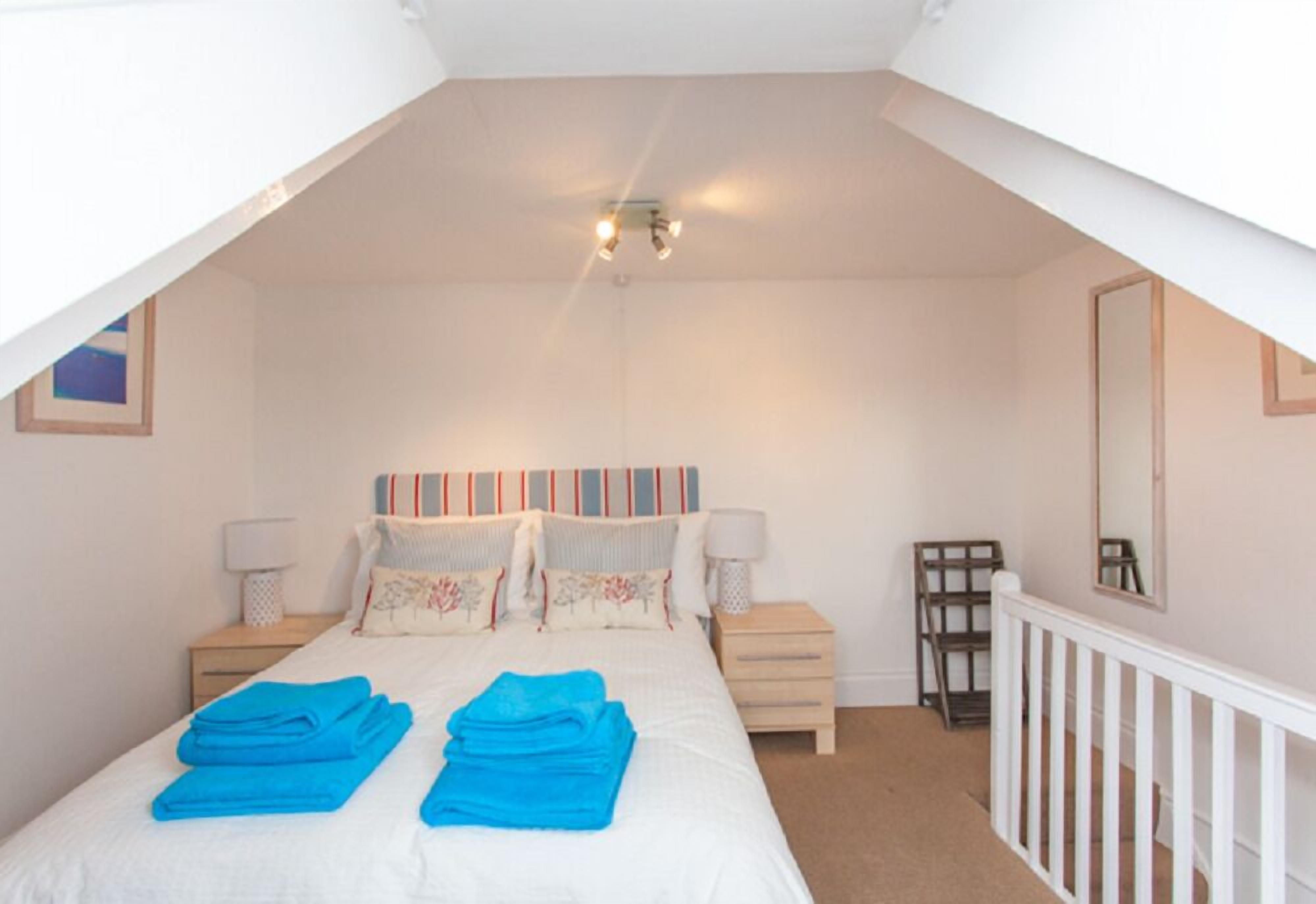A bedroom with a bed, two bedside tables, a nightstand, a crib, and a white railing.