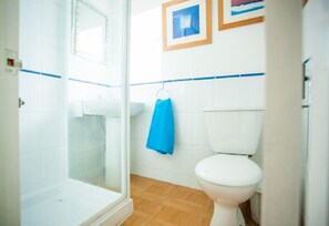 Une salle de bain avec une douche à parois de verre, des toilettes blanches et une serviette bleue accrochée au mur.