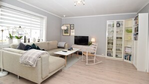 A modern living room with a sofa, coffee table, TV, and a bookshelf. - Solferie Holiday Apt. Johan Øydegards (Kristiansand)