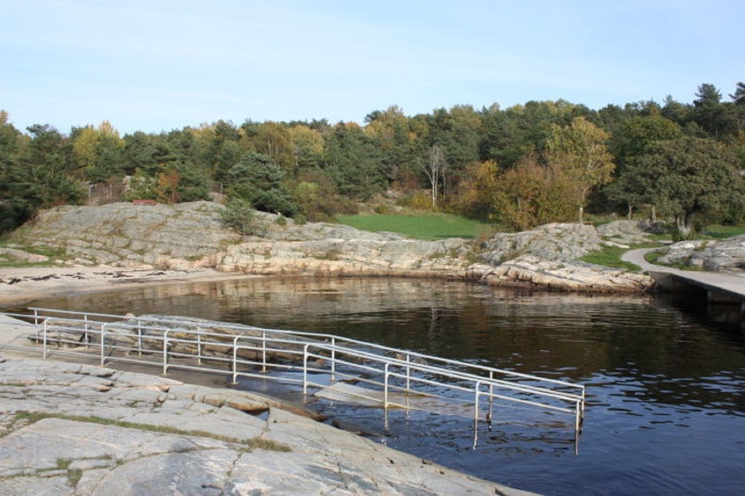 A rocky shoreline with a metal railing and a bridge over a body of water.