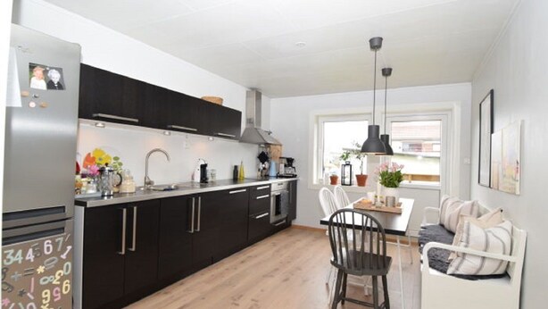 A modern kitchen with black cabinets, a stainless steel refrigerator, and a dining area with a white table and chairs. - Solferie Holiday Apt. Johan Øydegards (Kristiansand)