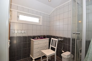A bathroom with a white vanity, a chair, a small window, and a shower area.