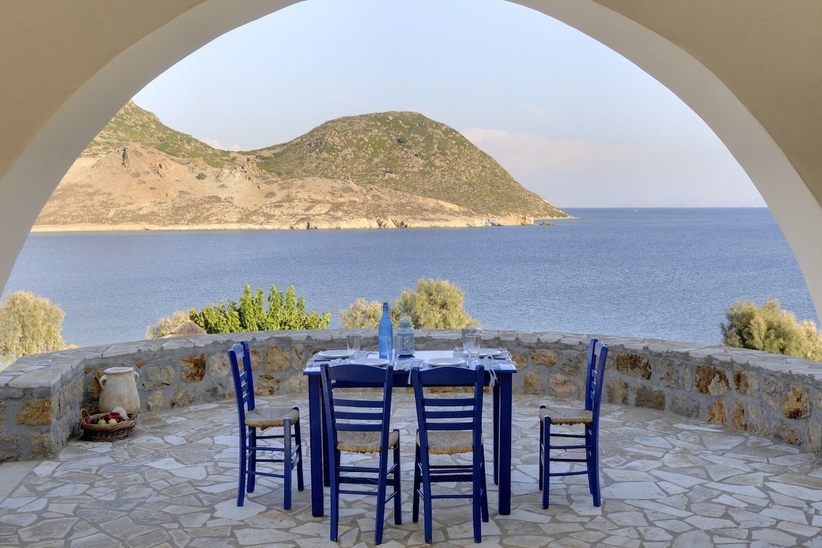 Mesa para cuatro personas con vista al mar y una colina al fondo.