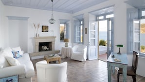 A spacious living room with a fireplace, white furniture, and large windows offering views of the outdoors. - Onar (Patmos)