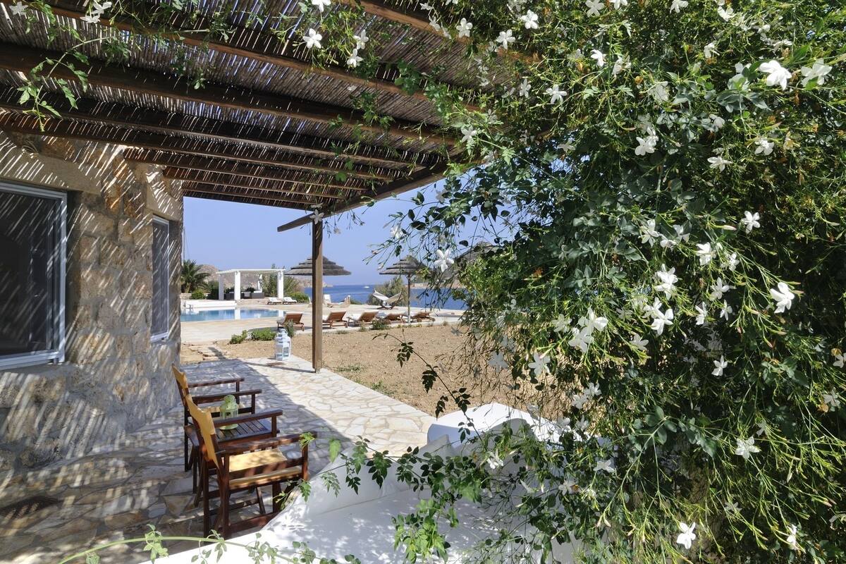 Un edificio de piedra con una pérgola de madera, asientos al aire libre y vista al mar.