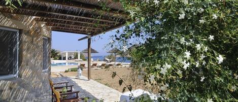 A stone building with a wooden pergola, outdoor seating, and a view of the sea.